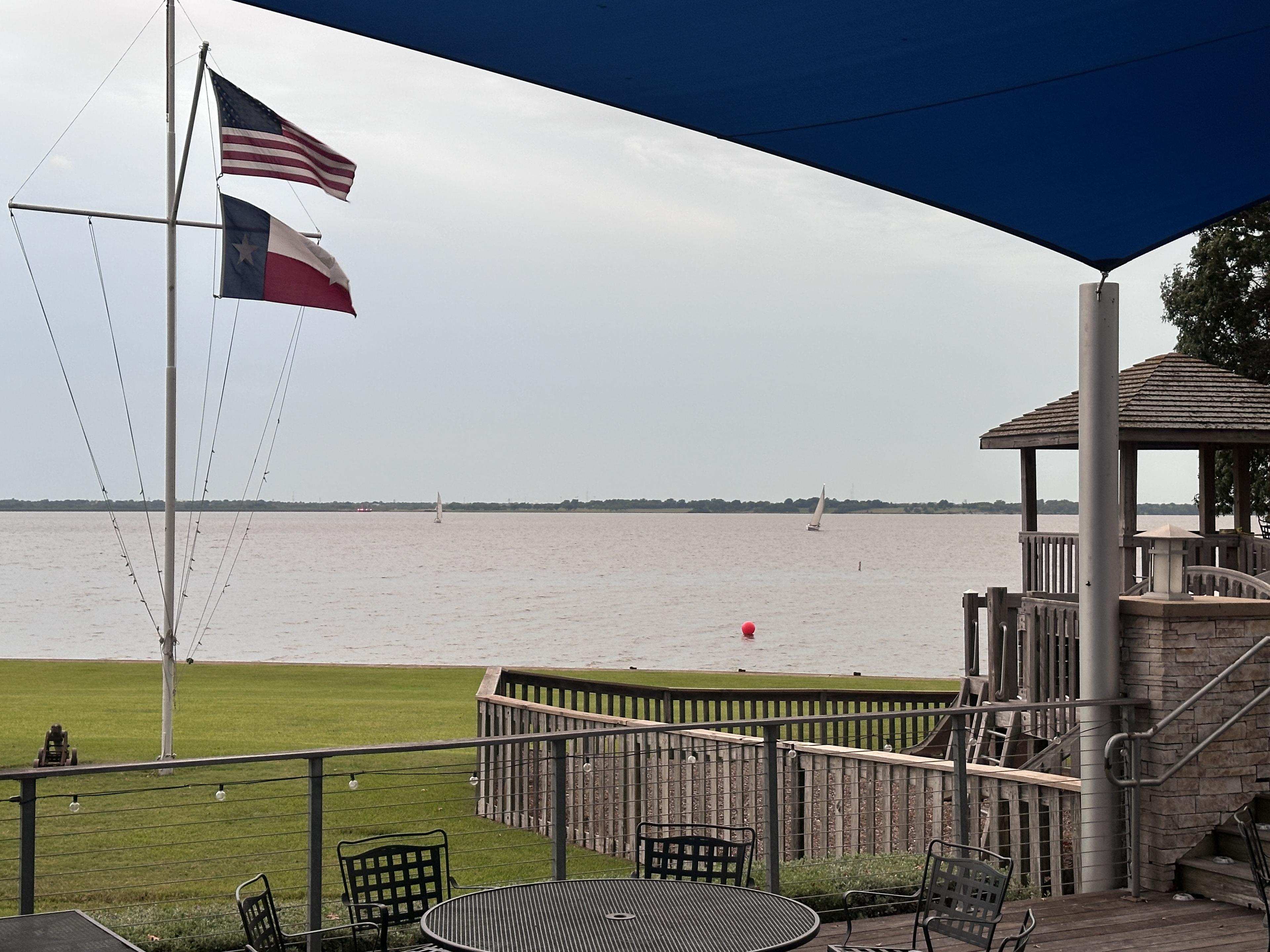 Rush Creek Yacht Club deck with US and Texas flags and sailboats on Lake Ray Hubbard